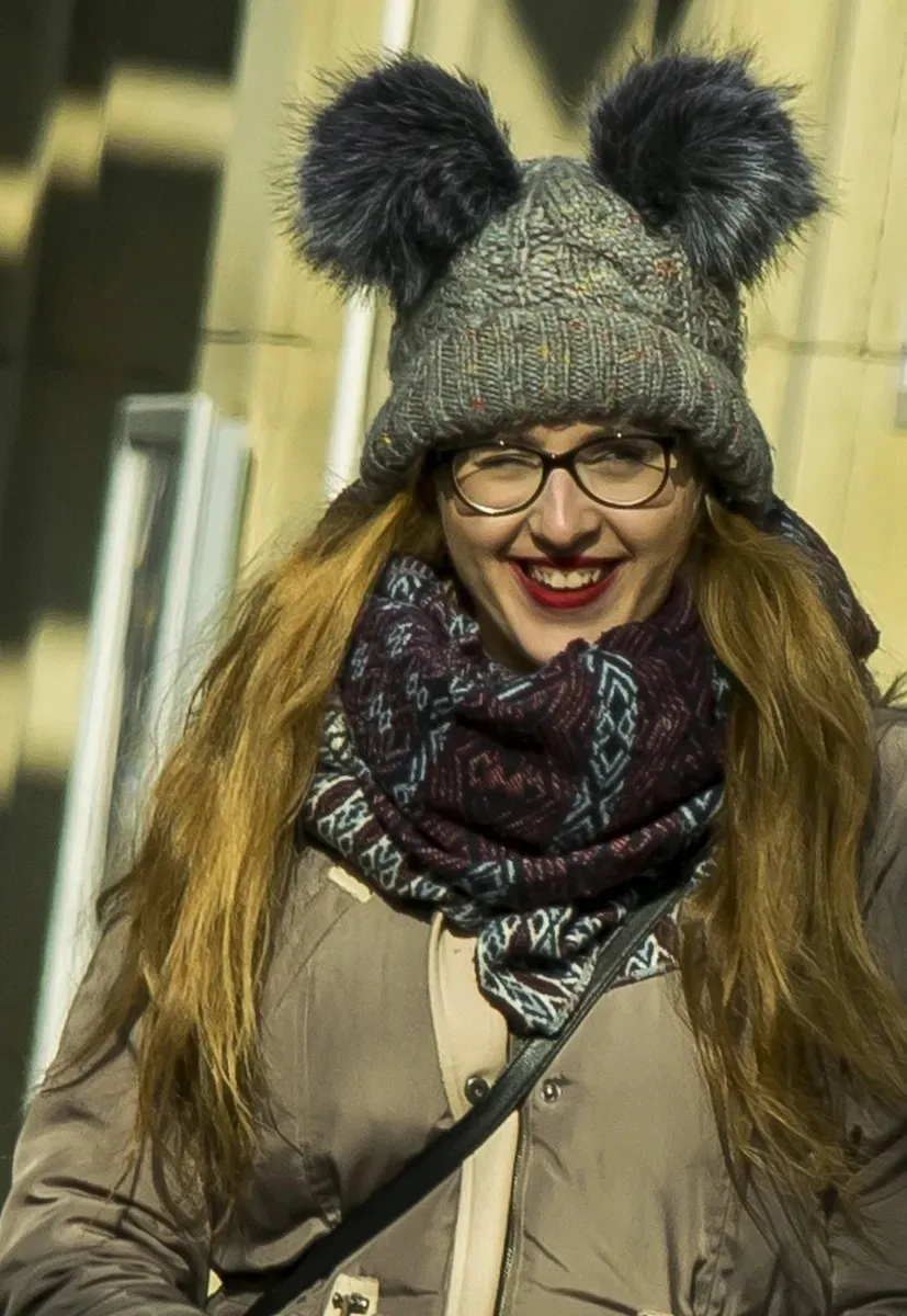 Smiling woman in glasses wearing a hat with pom-poms
